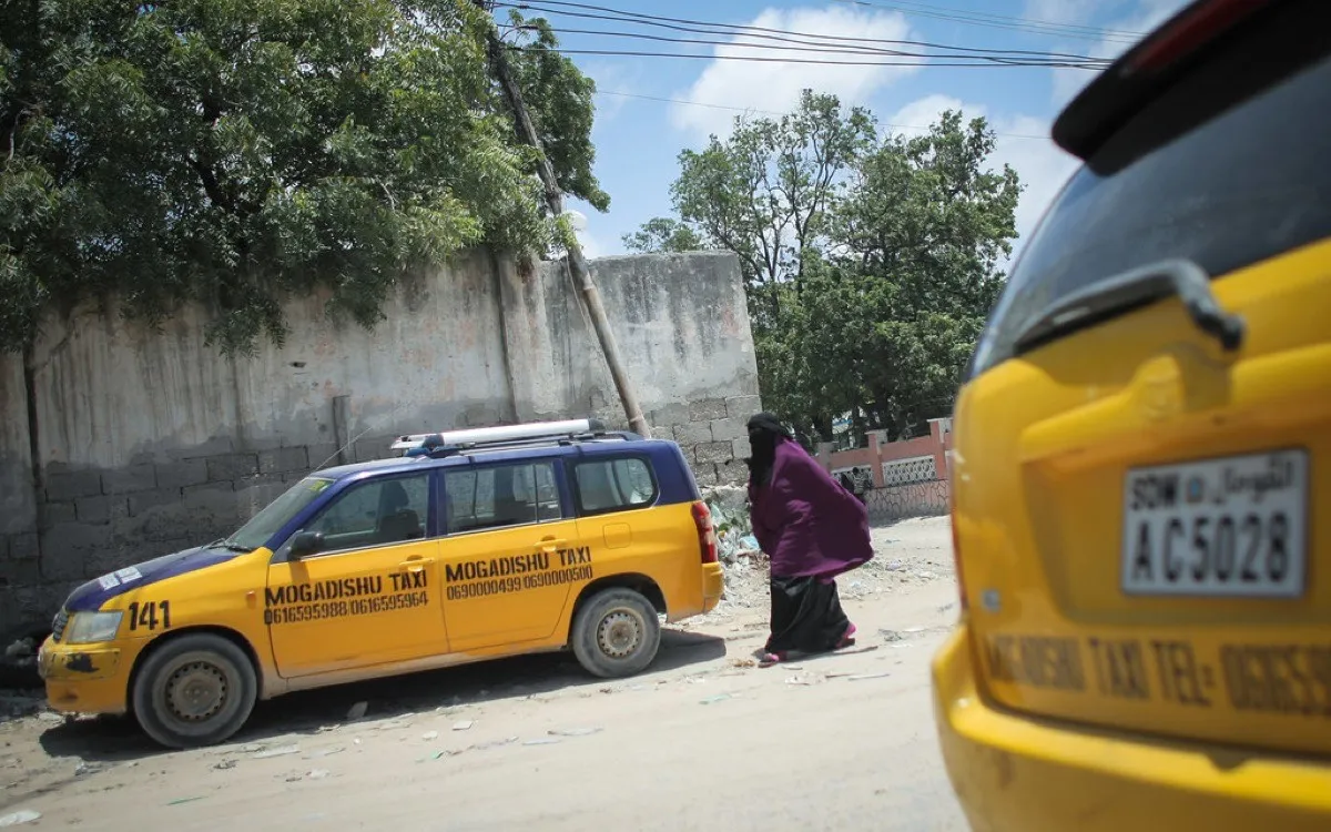 Yellow taxis parked on a roadside in Kangra, a woman walking past
