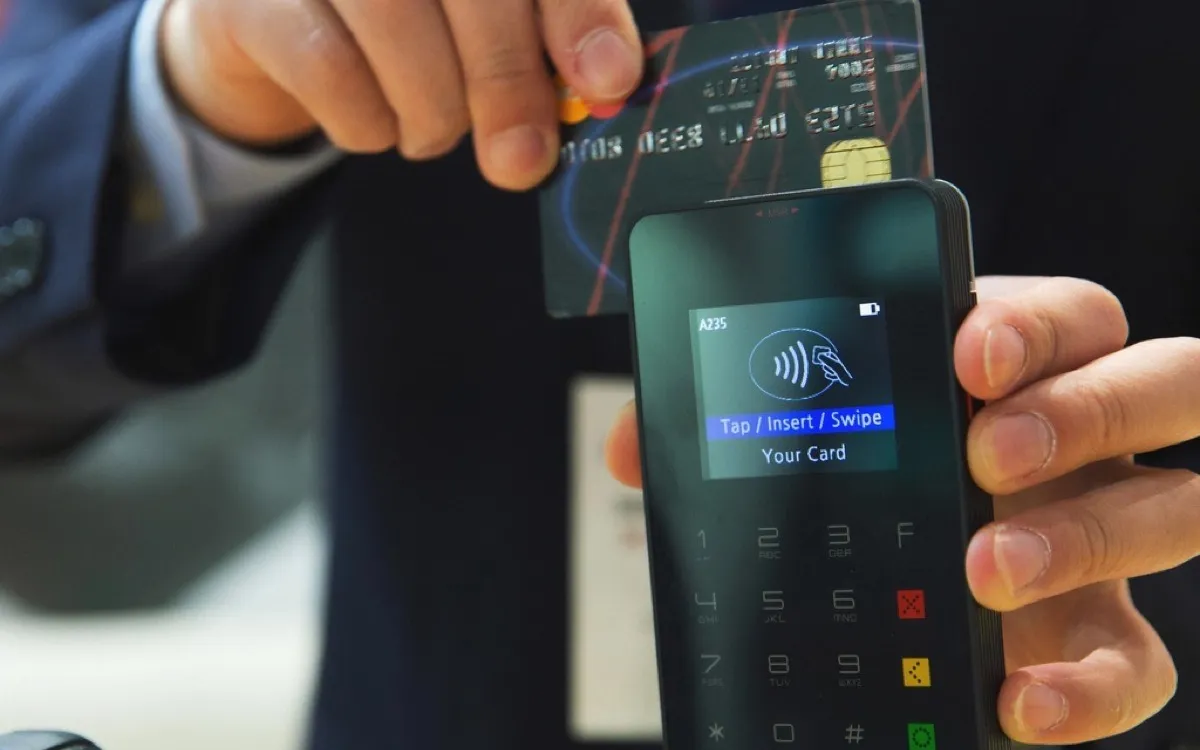 A customer tapping a bank card against a handheld card payment terminal