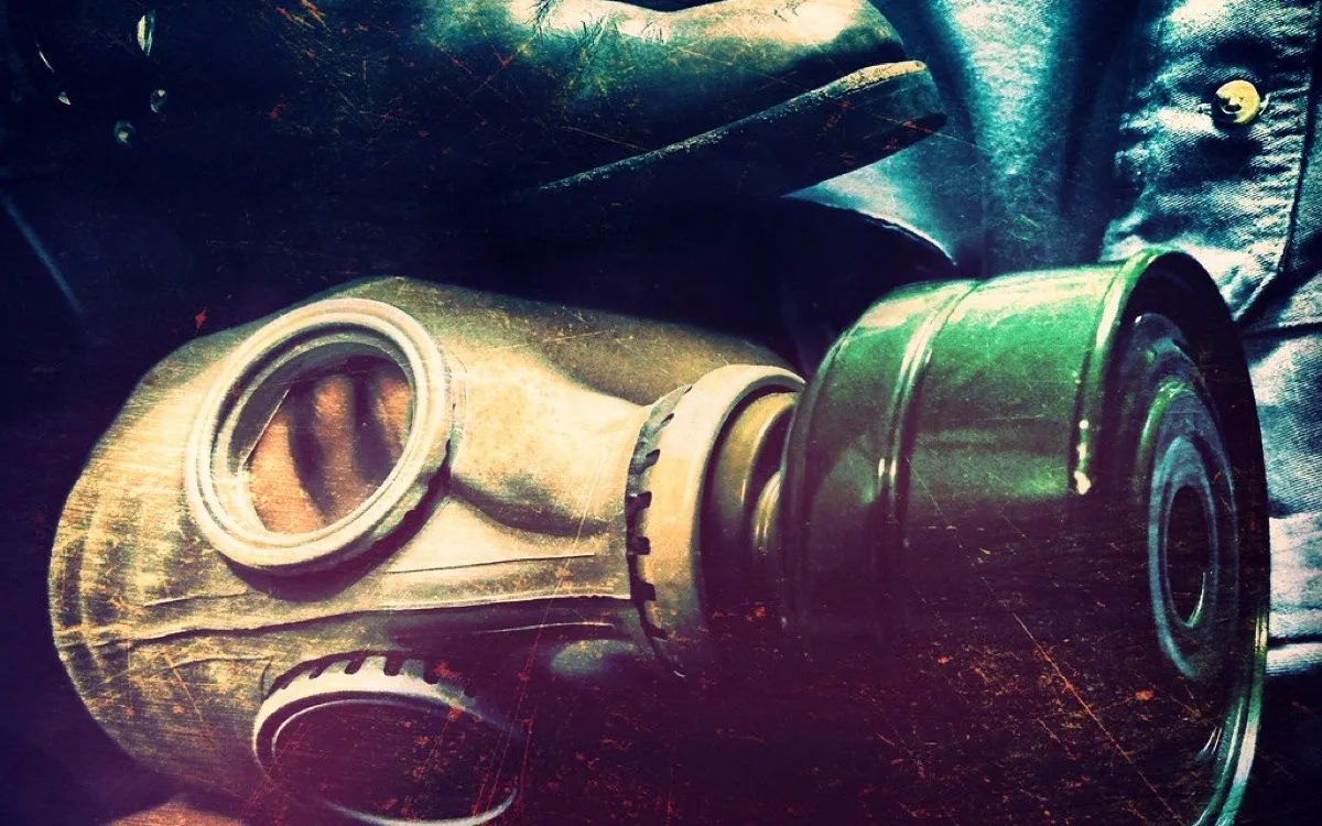 A vintage rubber gas mask lying on a wooden floor beside a denim jacket
